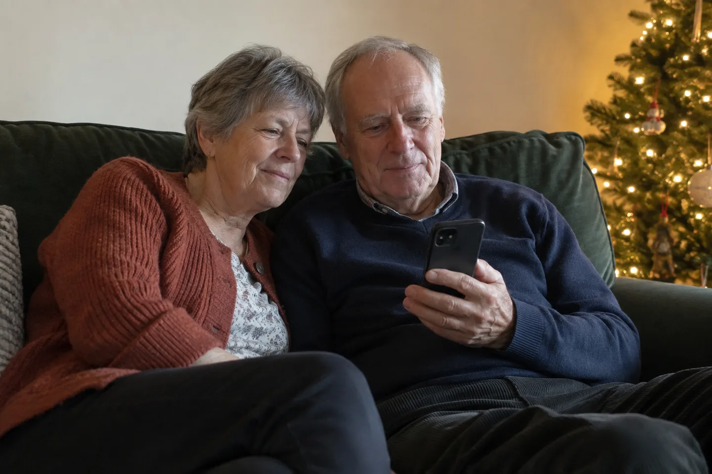 Mom and Dad sitting together by their Christmas tree, listening to a song on a phone