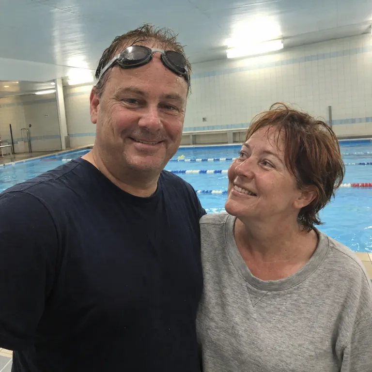 Daniel laughing beside a swimming pool with his wife, goggles resting on his head