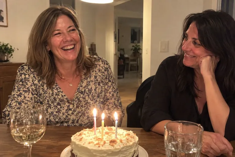 A woman celebrating her fiftieth birthday with a friend over cake at home