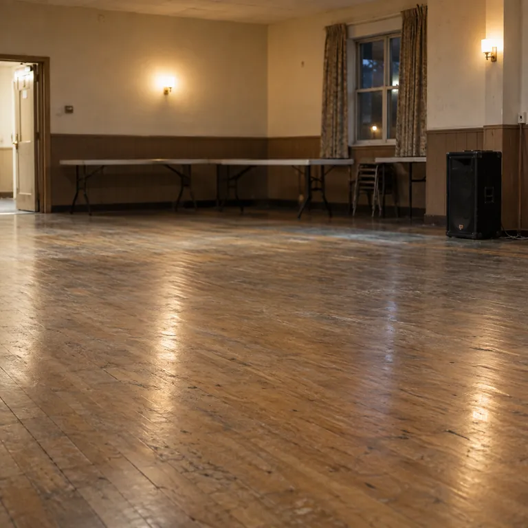 A wooden dance floor in a modest community hall with a speaker beside it