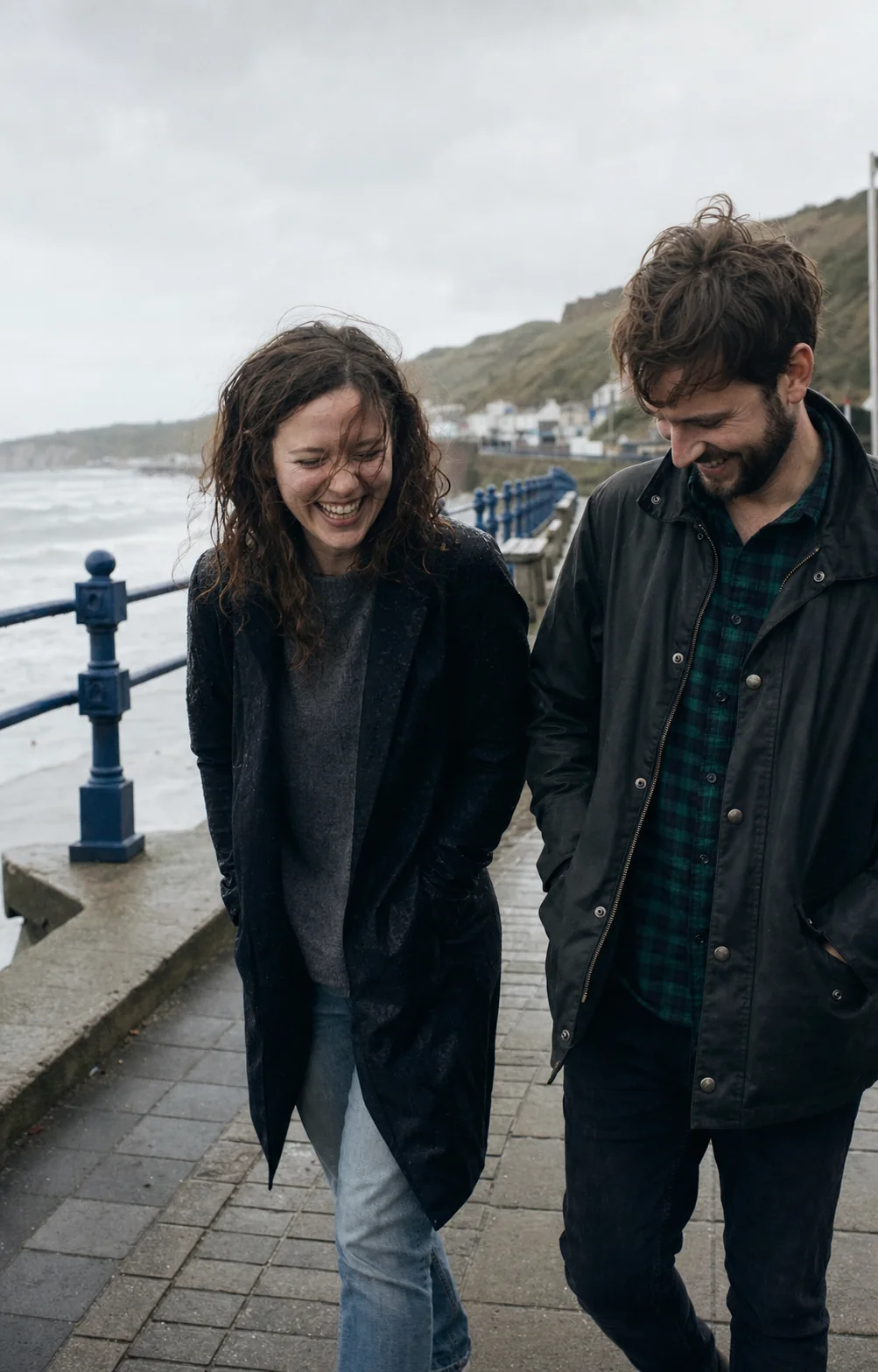 A couple laughing together on a rainy seaside walk