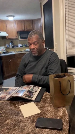A man at a kitchen table with a photo album and a gift bag listens, a real customer reaction