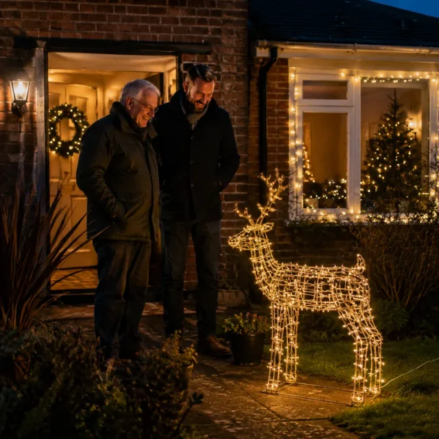A father and grown son beside a light-up Christmas reindeer in their front garden