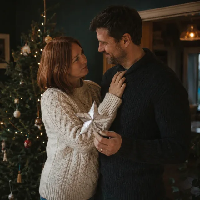 A couple holding a creased silver paper star beside their Christmas tree
