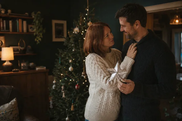 A couple holding an old paper star beside their Christmas tree