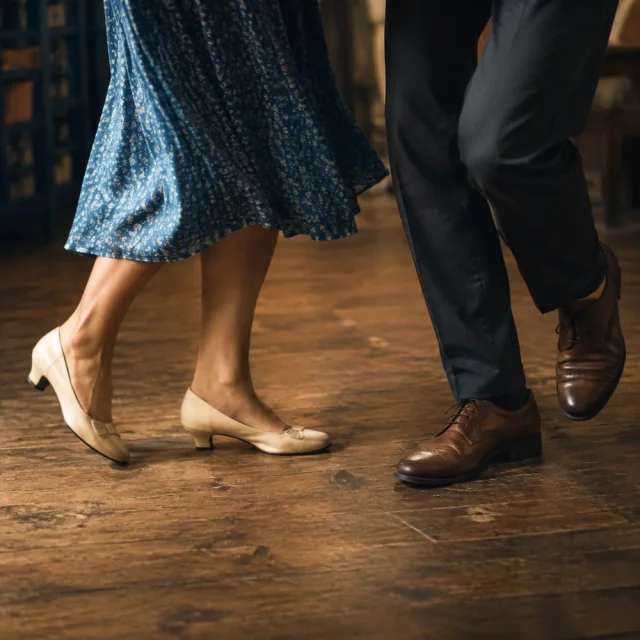 A couple in a blue dress and dark trousers taking an awkward dance step on a wooden floor