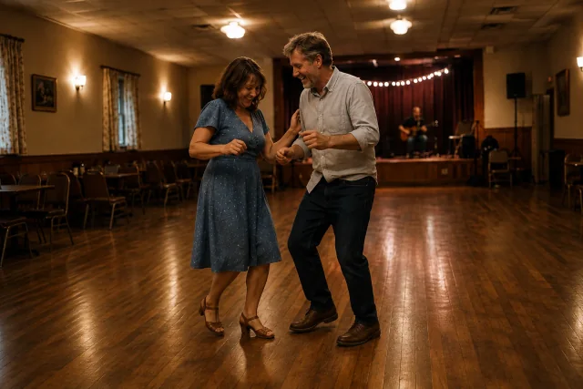 A married couple laughing as they dance together in a warmly lit community hall