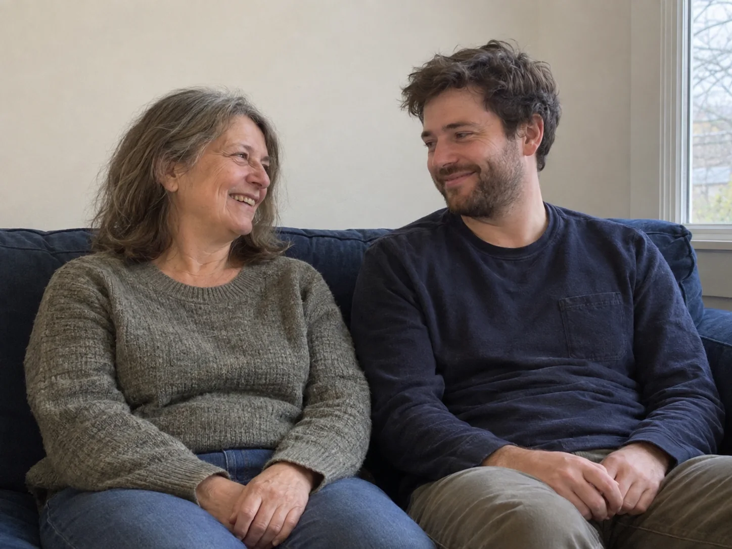 A mother and her adult son sharing a laugh on the sofa at home